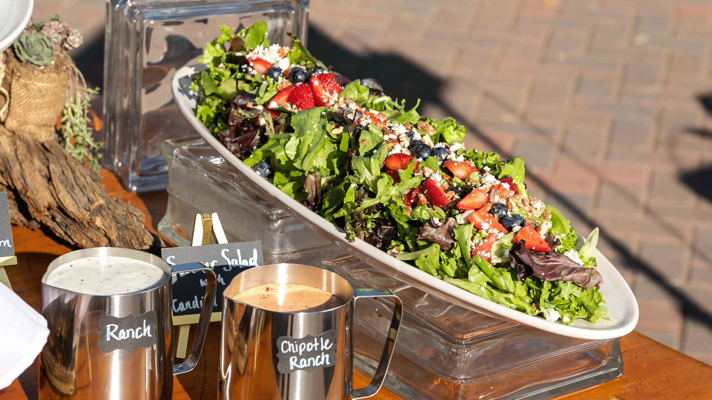 Mixed greens with strawberry salad sitting on a table with dressings in containers on the side